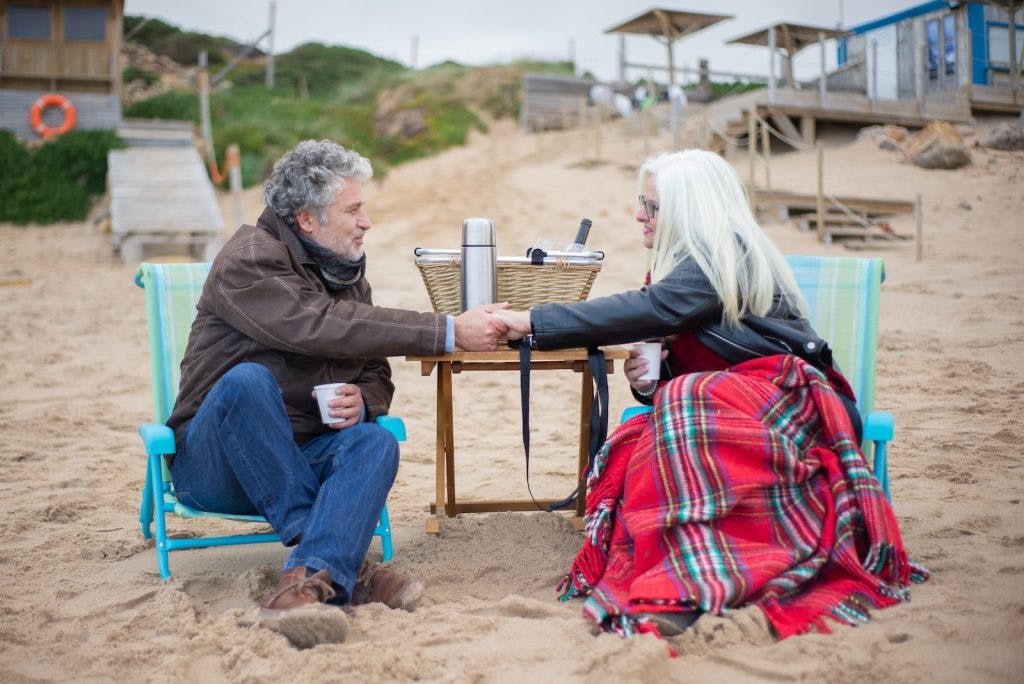 Photo of an Elderly Couple Holding Hands while Having a Picnic