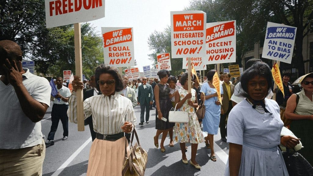 Demonstrators walk along a street holding signs demanding the right to vote and equal civil rights at the March on Washington