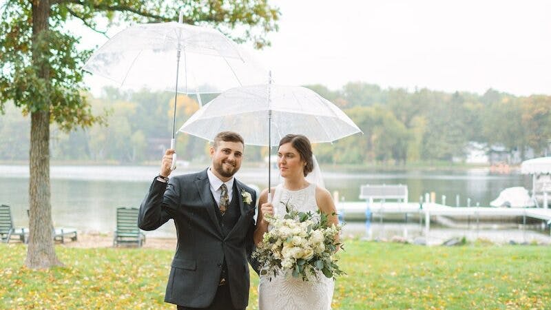 a bride and groom walking under an umbrella in rain