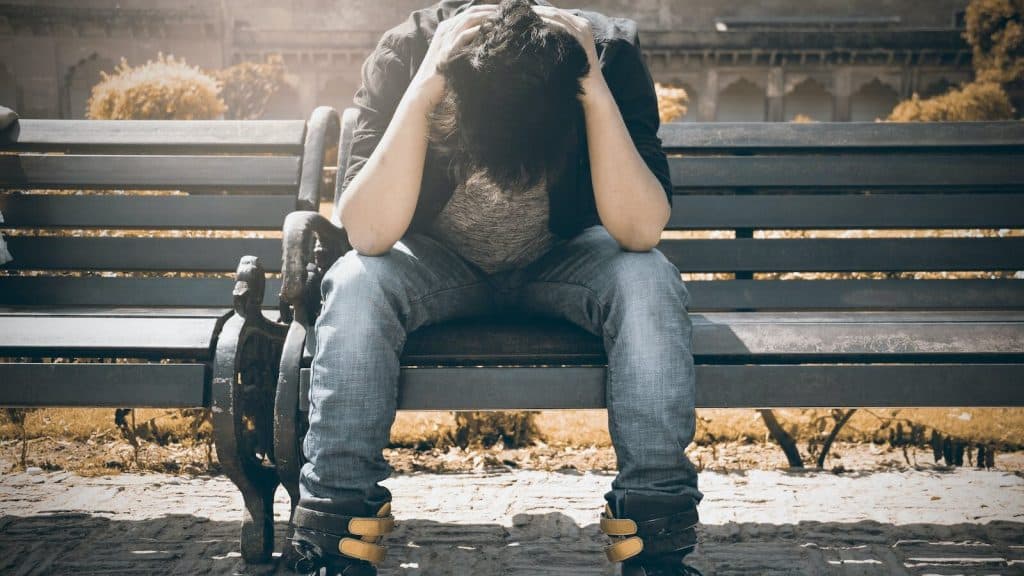 Man in Black Shirt and Gray Denim Pants Sitting on Gray Padded Bench
