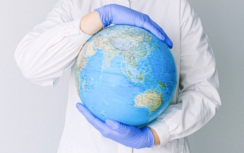 Person With a Face Mask and Latex Gloves Holding a Globe