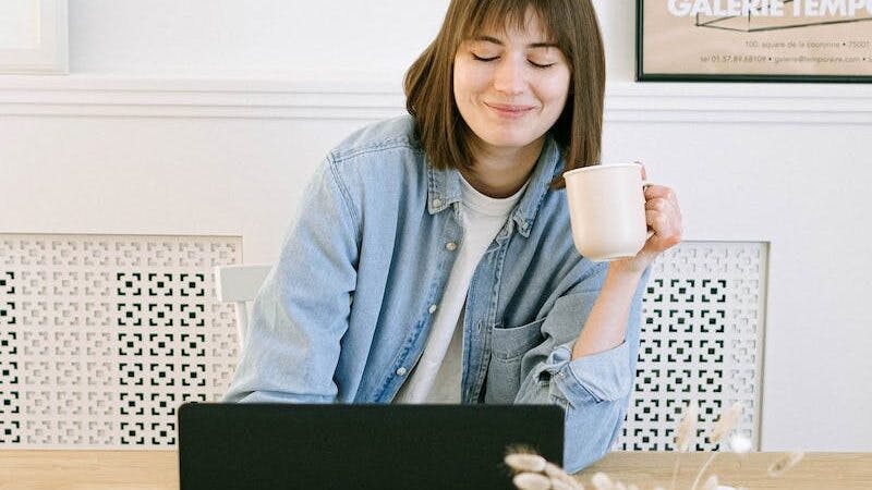 Woman Drinking Coffee and Looking at a Laptop