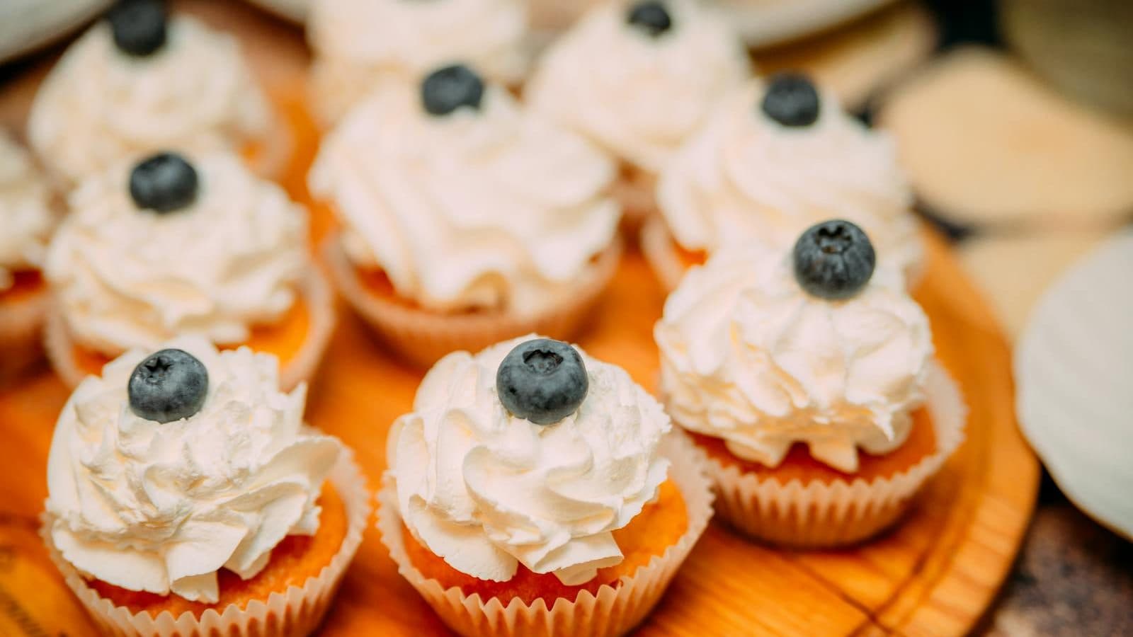 High angle of delicious cakes with creamy topping and berries placed on wooden plate on buffet table