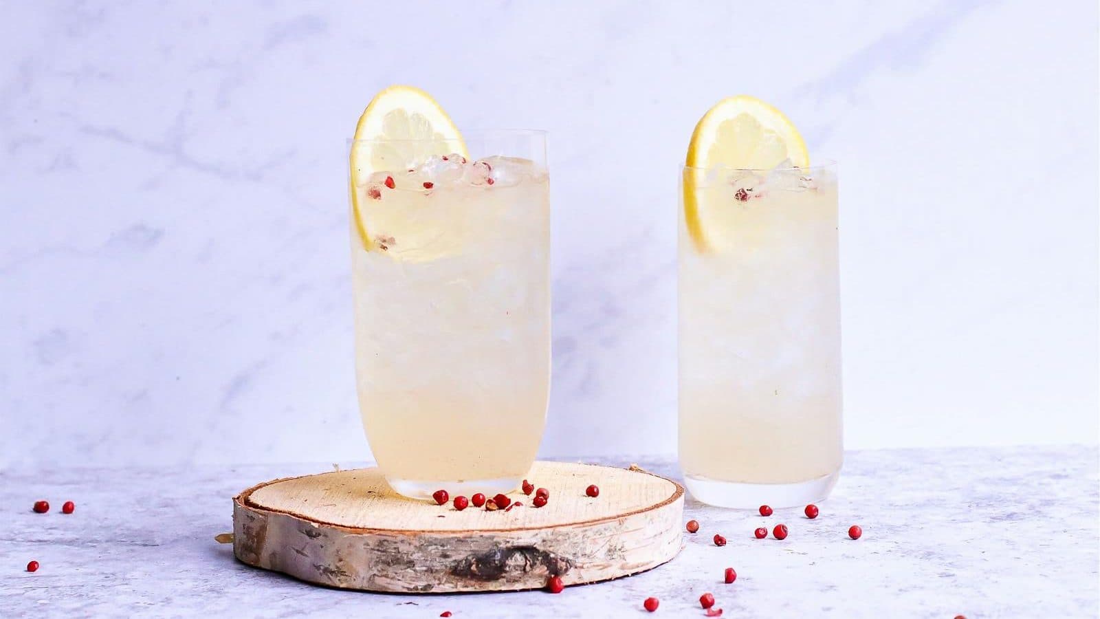 Glasses of delicious cold lemonade decorated with lemon slice and berries on wooden board in light studio