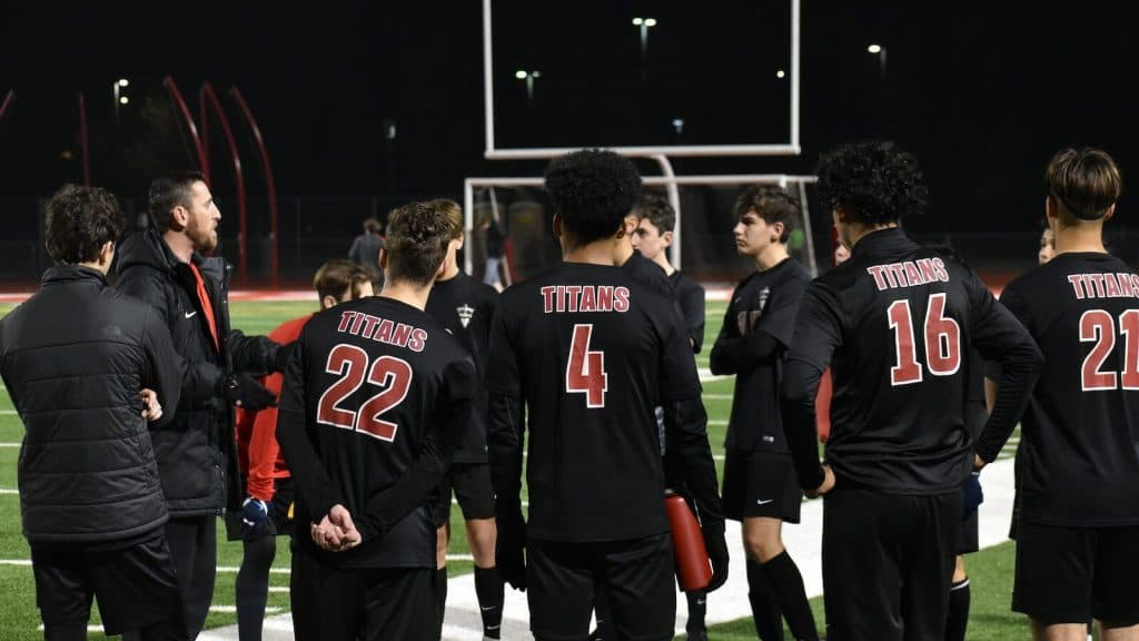 group of men in red and black jersey shirt standing on green grass field