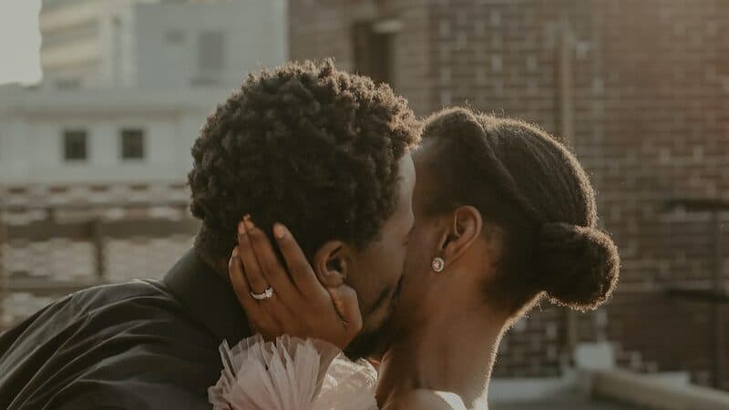 man in black leather jacket kissing woman in pink dress
