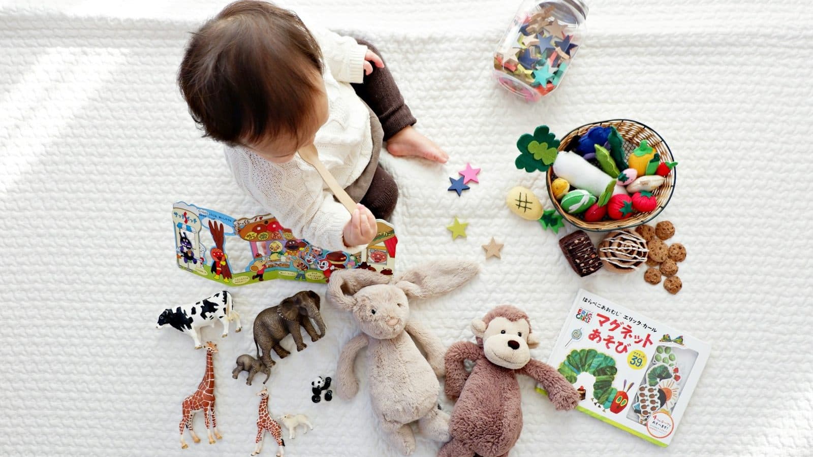 boy sitting on white cloth surrounded by toys