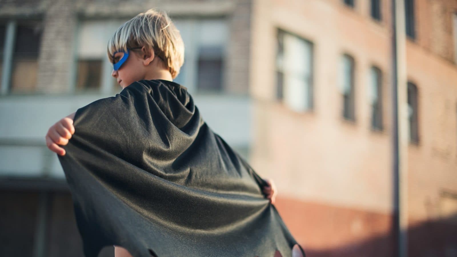 selective focus photography of boy wearing black Batman cape