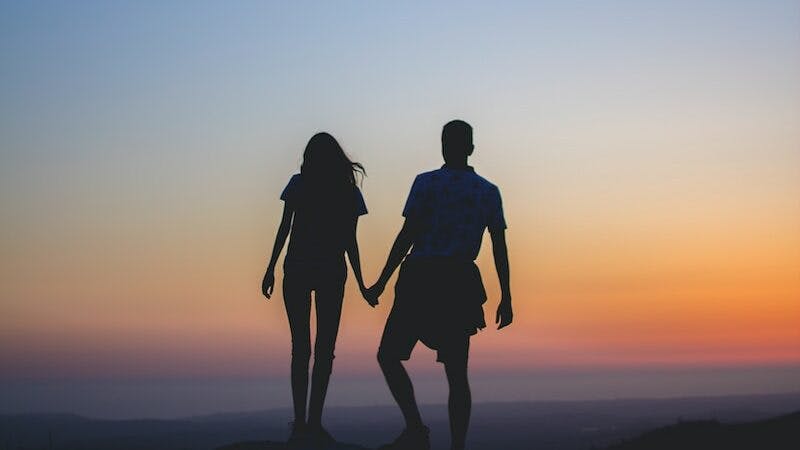 man and woman holding hands in silhouette photography