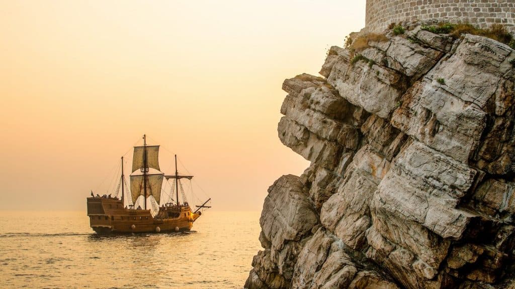 a boat sailing on the water near a rocky cliff